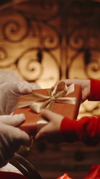 Santa Claus hands gift to child by fireplace, Christmas magic and holiday giving concept, vertical slow motion