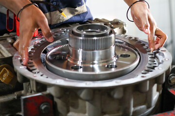 Fototapeta premium ​A mechanic's hand carefully places a clutch reaction plate into a complex transmission assembly during a detailed engine repair or maintenance process.