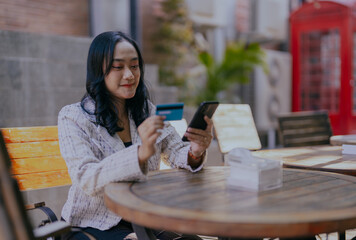 Woman, smartphone and credit card at a restaurant in the outdoor with checking for finance. Cheerful asian young female paying and mobile for online payment at cafe in nature on an app with technology
