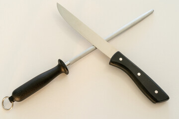 Knife and blade sharpener lying diagonally over each other, on a white canvas.