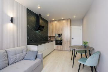 Modern kitchen and living room blend with a sofa, dining table, stylish cabinets, and black marble backsplash