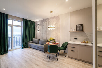 modern living space with a sofa, dining table, and kitchenette, featuring green accents and natural light