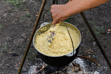 Close-up top view of porridge being stirred in a cauldron over an open fire with a wooden spoon, authentic outdoor rustic cooking scene