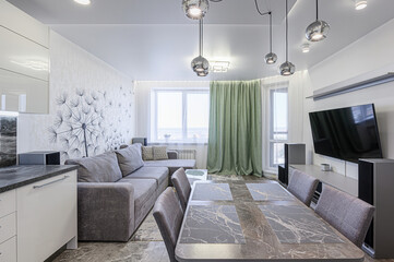 Modern living room with a gray sofa, dining table, and TV. Accented by unique pendant lights and a dandelion wall design