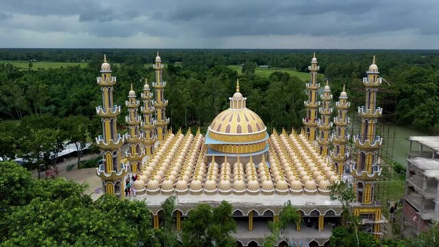 Tangail, Bangladesh - 22 August 2025: Aerial view of the 201 Dome Mosque, a golden architectural marvel rising amidst lush green trees under a cloudy sky.