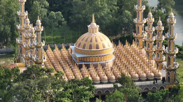 Tangail, Bangladesh - 22 August 2025: Aerial view of the vibrant 201 Dome Mosque, its golden domes contrasting against the lush greenery and serene waters.