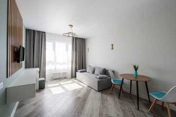 Modern apartment interior with sofa, table, chairs, TV, and natural light. Minimalist design, clean lines