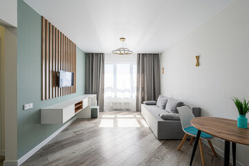 Modern apartment interior with sofa, table, chairs, TV, and natural light. Minimalist design, clean lines
