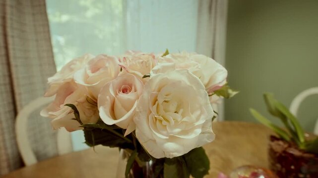 Close-up of a bouquet of pale pink and white roses in a glass vase on a wooden table, soft daylight from the window creates a warm romantic atmosphere, perfect for weddings or decor themes