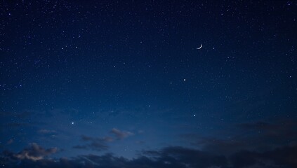 Fototapeta premium A crescent moon glows among countless stars within the deep blue night sky, featuring faint clouds near the horizon adding depth to the tranquil celestial scene