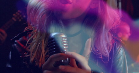 Singing singer wearing leather jacket gripping vintage mic onstage with electric guitar lights