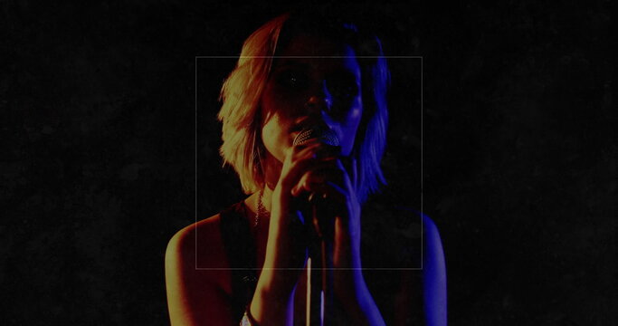 Performing teenage female singer gripping handheld microphone on dark stage, with red blue lighting