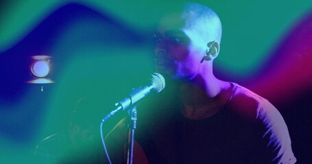 Singing male singer using mic stand under spotlight at club stage, with colored lighting projectors