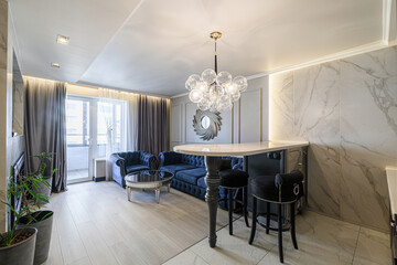 Stylish interior. Blue velvet sofa chairs. Modern chandelier, marble wall, light wood floors. Balcony view. Elegant bar area with stools