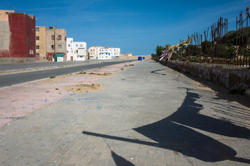 Street at the edge of Essaouira, Morocco. Rusty fence, drying laundry casting shadows on the...