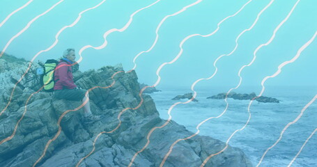 Sitting hiker surveying choppy sea at coastal cliff, with yellow backpack, water bottle, copy space