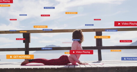 Woman wearing sportswear doing backbend on lakeside dock, with yoga mat, railing, digital banners