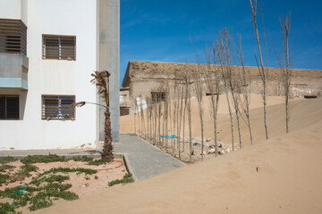 Outskirts of Essaouira, Morocco. Sand dune encroaching on a sidewalk between residential buildings....
