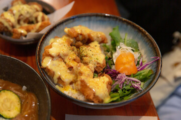 Crispy fried chicken with creamy yellow sauce on rice, served with fresh salad of greens and shredded vegetables in deep ceramic bowl on table