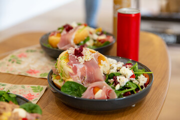 Colorful salad bowl with soft sandwich topped with prosciutto, feta crumbles, and beetroot served on wooden table with floral napkins and soda