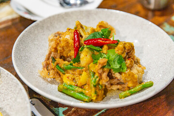 Stir-fried seafood with curry sauce, red chili and green beans served in ceramic bowl, spicy Thai dish in cozy restaurant on wooden table setting