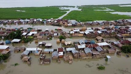 Bogura, Bangladesh - 22 August 2025: Aerial view of a flooded village, with homes submerged in murky water and green vegetation contrasting with the grey sky.