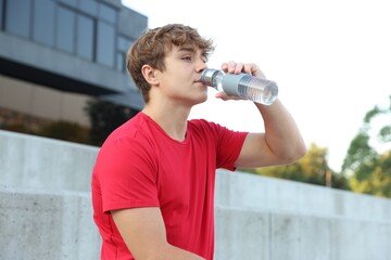 Teenage boy drinking water after training outdoors