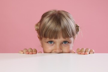 Curious little girl peeking over table against pink background