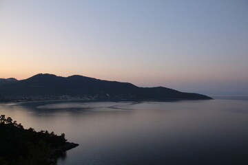 Obraz premium A wide-angle landscape of a bay or lake with a mountain in the background at dusk, showing a calm, serene body of water reflecting the soft light of the sky.