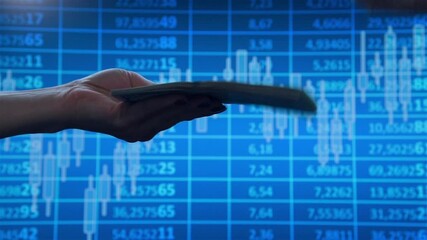 Hand extends a large wad of .dollars to another hand against the background of business charts on screen. Slow Motion Effect.