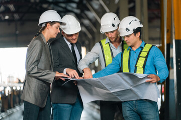 Engineers wearing safety helmets inspecting railway blueprint beside a vintage locomotive, symbolizing teamwork, innovation, and development in modern rail transportation and infrastructure projects