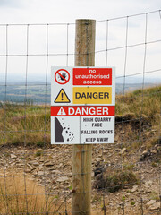 Warning sign indicating risk and danger of falling rocks near a quarry edge.