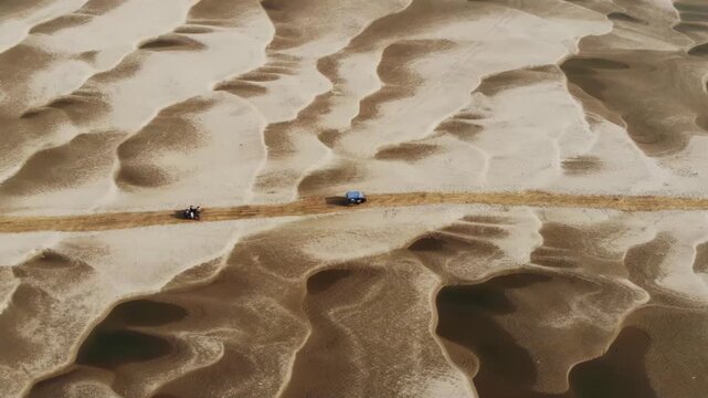 Bogura, Bangladesh - 22 August 2025: Aerial view of a motorcycle and car traversing a sandy path through undulating dunes with contrasting light and dark tones.