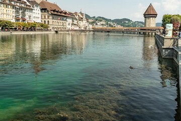 Chapel Bridge - a wooden footbridge in the city of Lucerne in Switzerland with a water tower in a sunny day, from the perspective of the Reuss river.