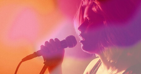 Teen singer performing in strappy top with mic on stage, with colored lights, haze, copy space