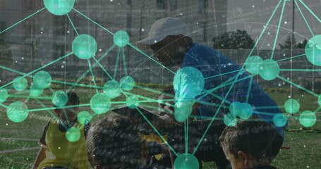 Coaching blue shirted, white capped coach kneeling on turf, with soccer cones, ball and spheres