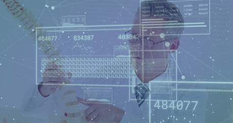 Holding spinal column model, mature doctor in lab coat analyzing holographic data panels in clinic