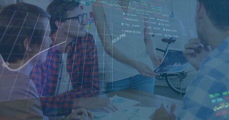 Standing project manager explaining data in meeting room, with printed charts and data overlays