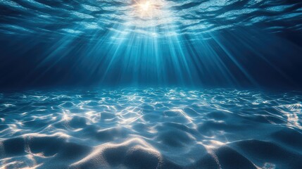 Underwater scene showcases sunlight rays penetrating the deep blue water, illuminating the sandy bottom.  Light beams create a dramatic effect on the textured seabed.