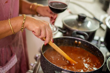 Chef preparing red meat sauce for ravioli with glass of wine