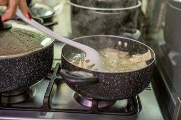 Chef preparing ravioli in boiling water with red meat sauce cooking in pot on stove