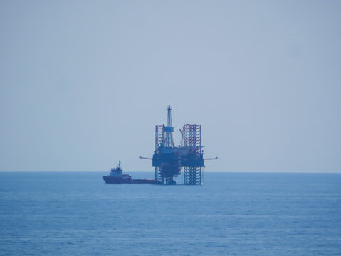 Offshore oil drilling platform with offshore supply vessel (OSV) alongside, operating in open sea for energy and petroleum industry support.