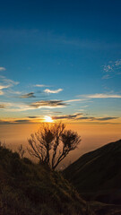 The sun rises over the mountain, silhouetted by the valley.