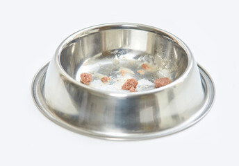 close up of a stainless steel pet bowl with remaining wet food pieces on a white background.