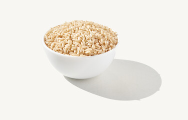 White bowl filled with uncooked brown rice isolated on light background.