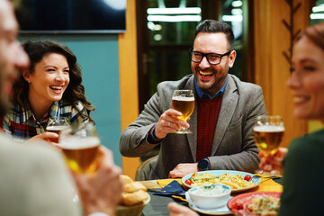 Cheerful friends raising beer glasses enjoying a meal together at a restaurant, laughing and celebrating