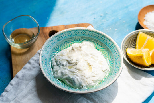 Close-up of a bowl of Traditional tzatziki with sea salt and lemons on a blue wooden table