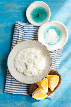 Overhead view of a bowl of Traditional tzatziki with sea salt and lemons on a blue wooden table