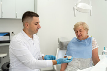 Fototapeta premium dentist consulting a retired woman with the installation of a tooth crown, an implant. Artificial teeth with steel pin