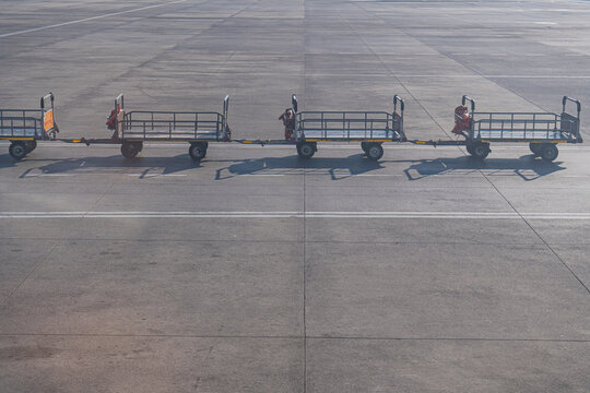 Empty luggage carts on an airport runway waiting for a plane to land